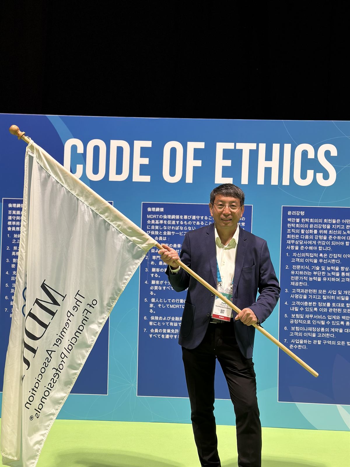 Frank Zhou holding the MDRT flag in front of the Code of Ethics wall at the MDRT Global Conference